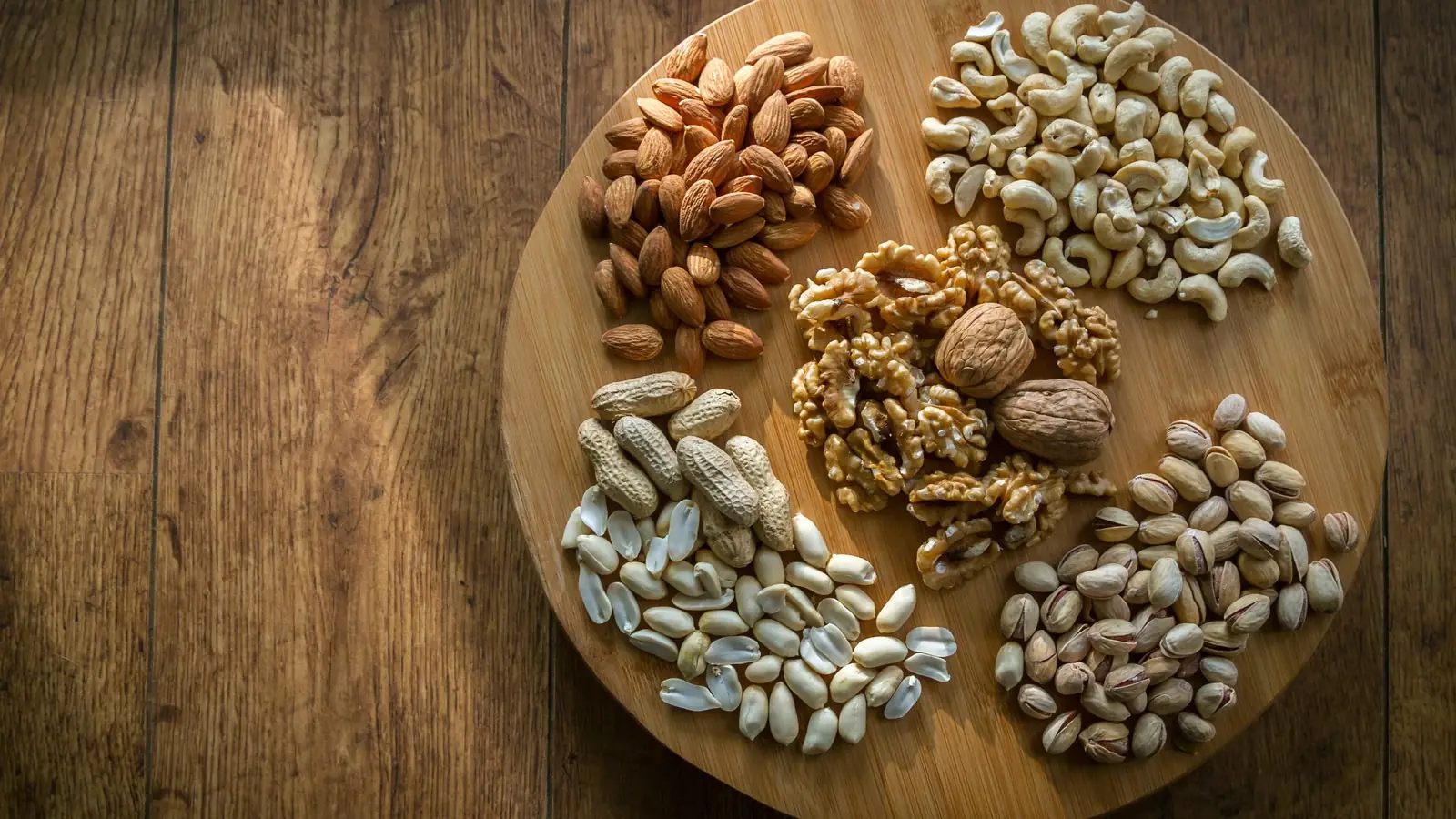 Assorted premium nuts — almonds, cashews, walnuts and pistachios on a wooden board